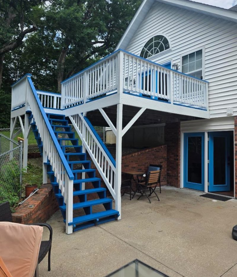 Deck repairing project featuring an elevated backyard deck with blue stairs, white railings, patio doors, and a restored outdoor seating area.